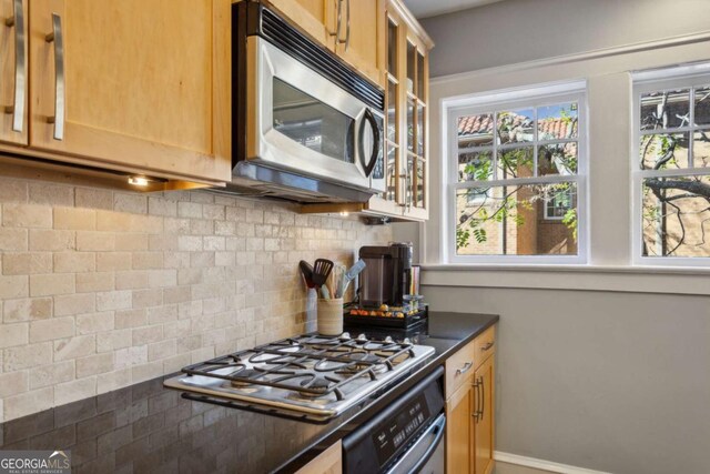 kitchen with stainless steel appliances, dark countertops, tasteful backsplash, glass insert cabinets, and baseboards