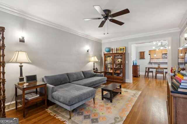 living area with a ceiling fan, crown molding, baseboards, and wood finished floors