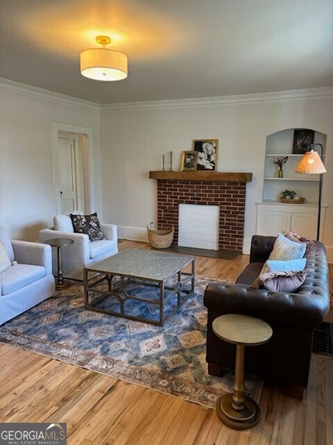 living area with a brick fireplace, baseboards, ornamental molding, and wood finished floors