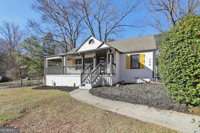 view of front of house featuring covered porch, roof with shingles, a front yard, and fence