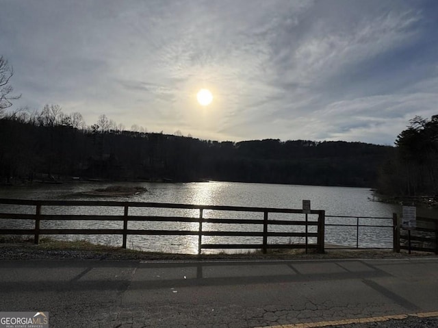 view of dock with a water view, fence, and a wooded view