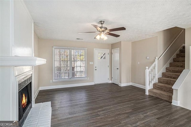 entryway with dark wood-style flooring, stairway, a textured ceiling, a warm lit fireplace, and baseboards