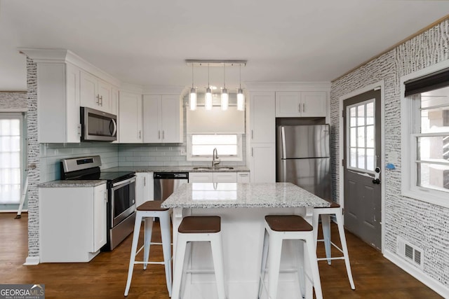 kitchen with stainless steel appliances, pendant lighting, white cabinetry, and a kitchen island