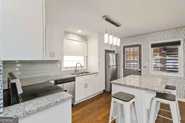 kitchen with white cabinets, appliances with stainless steel finishes, a center island, hanging light fixtures, and a sink