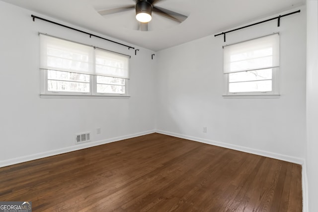 empty room with dark wood-style floors, plenty of natural light, visible vents, and a ceiling fan