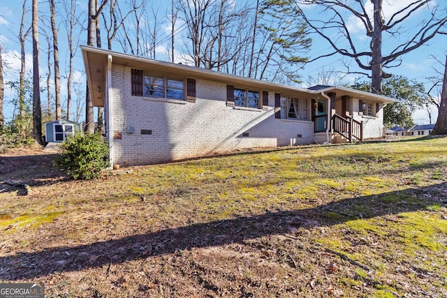 view of front of house featuring a storage shed, an outbuilding, crawl space, a front lawn, and brick siding