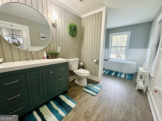 bathroom featuring toilet, wainscoting, vanity, wood finished floors, and a freestanding tub