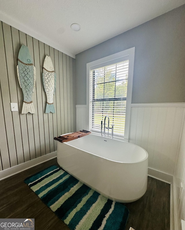 full bath featuring a freestanding tub, a wainscoted wall, and wood finished floors