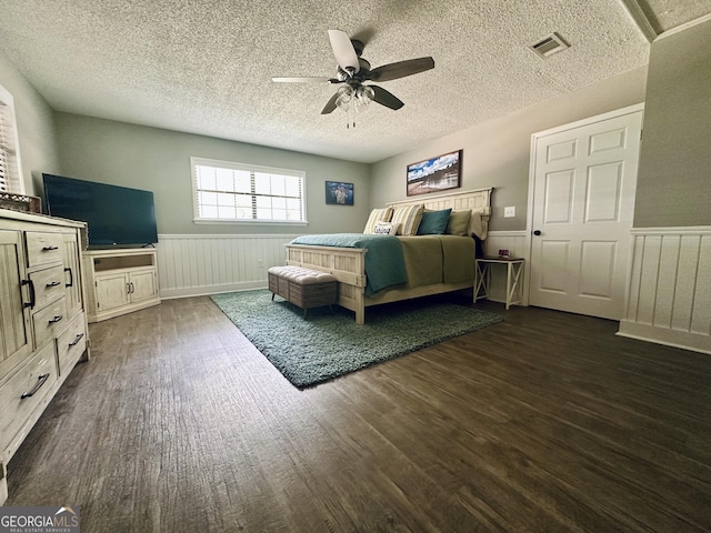 bedroom with a wainscoted wall, dark wood-style flooring, visible vents, and a ceiling fan