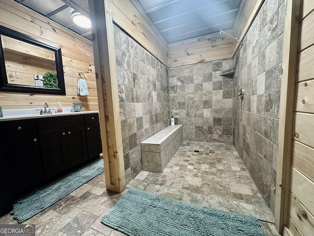 bathroom featuring stone finish flooring, tiled shower, wood walls, and vanity