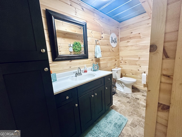 bathroom with stone finish flooring, vanity, toilet, and wooden walls