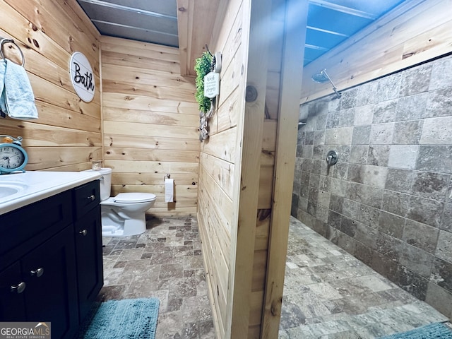 bathroom featuring stone finish floor, toilet, wooden walls, and vanity