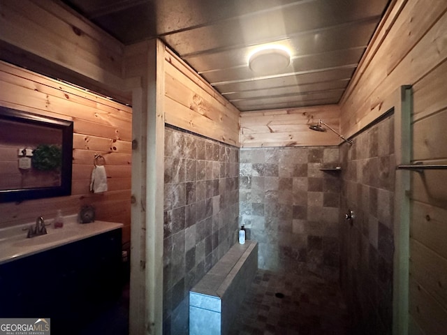 full bath with a tile shower, wooden walls, and vanity