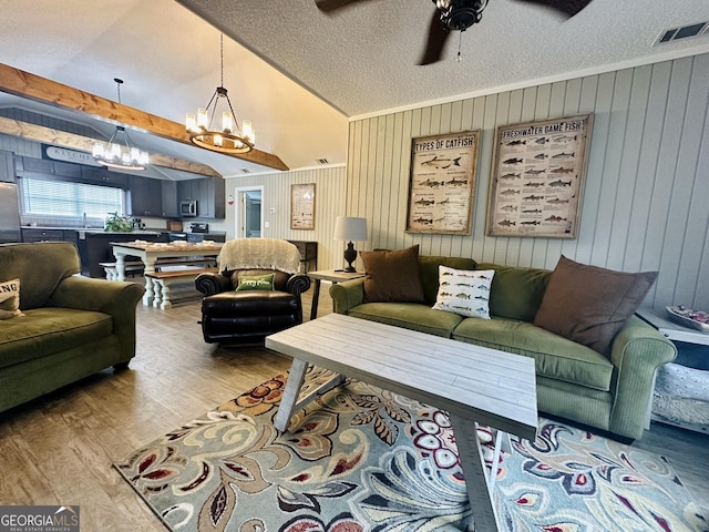 living area with visible vents, lofted ceiling with beams, wood finished floors, a textured ceiling, and ceiling fan with notable chandelier