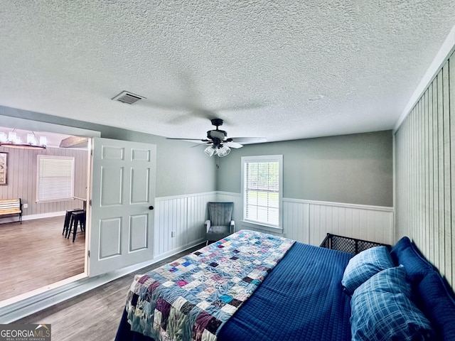 bedroom featuring a wainscoted wall, a textured ceiling, visible vents, and wood finished floors