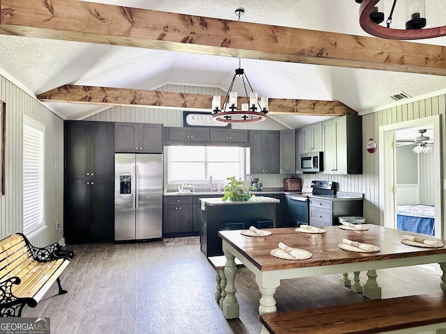 kitchen with a textured ceiling, vaulted ceiling with beams, stainless steel appliances, gray cabinets, and decorative light fixtures