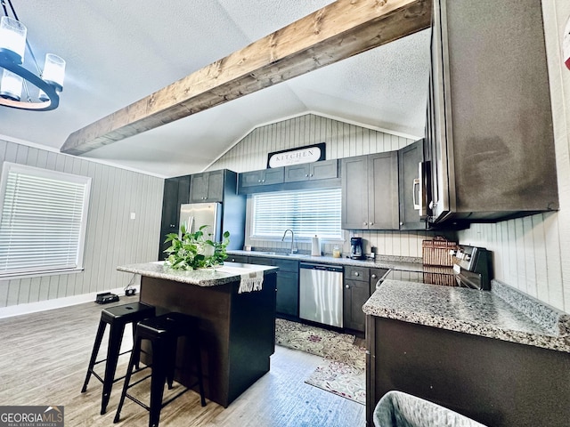 kitchen with lofted ceiling with beams, a breakfast bar area, a kitchen island, appliances with stainless steel finishes, and light wood finished floors