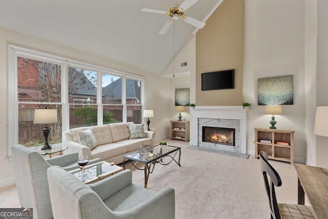 living area with baseboards, ceiling fan, carpet, high vaulted ceiling, and a high end fireplace