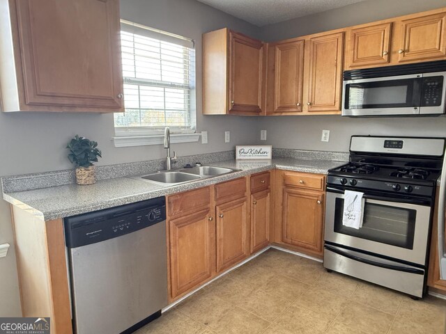 kitchen with stainless steel appliances, brown cabinetry, light countertops, and a sink