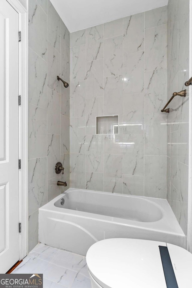 bathroom featuring toilet, marble finish floor, and bathing tub / shower combination