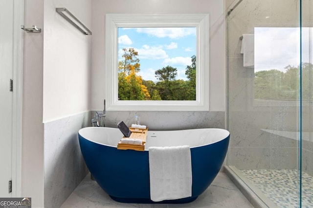 bathroom with marble finish floor, tile walls, a wainscoted wall, and a soaking tub