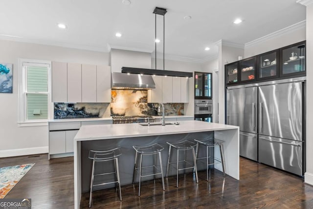 kitchen with a kitchen island with sink, stainless steel appliances, a sink, glass insert cabinets, and pendant lighting