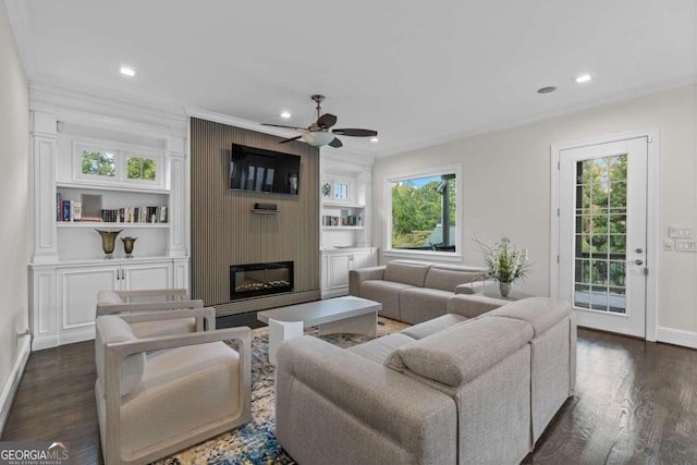 living area with dark wood-style floors, built in features, ornamental molding, a large fireplace, and baseboards