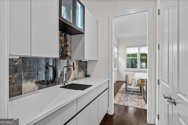 kitchen with tasteful backsplash, dark wood-type flooring, white cabinetry, a sink, and light stone countertops