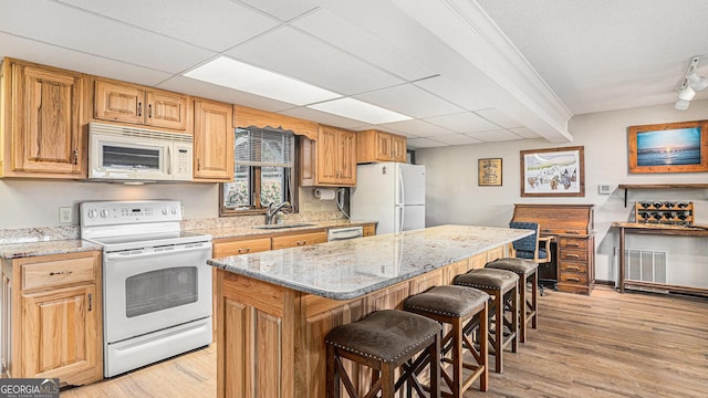 kitchen with white appliances, light stone counters, a center island, a kitchen bar, and a sink