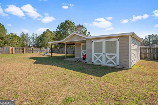 view of shed featuring a carport, a playground, and a fenced backyard