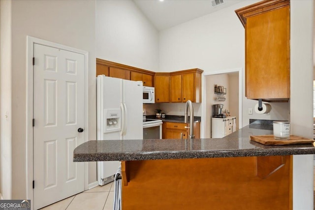 kitchen with a peninsula, white appliances, light tile patterned flooring, and a breakfast bar