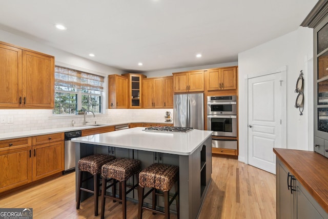 kitchen featuring a breakfast bar area, a sink, appliances with stainless steel finishes, a center island, and glass insert cabinets