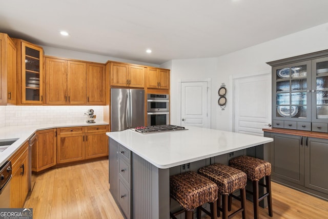 kitchen with a breakfast bar, a kitchen island, light countertops, appliances with stainless steel finishes, and glass insert cabinets