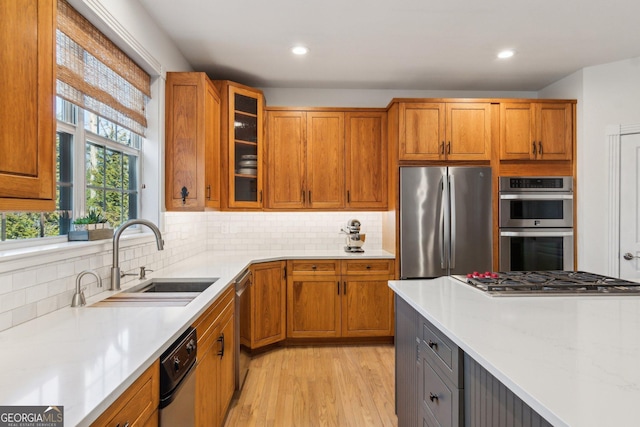 kitchen with light wood finished floors, tasteful backsplash, glass insert cabinets, appliances with stainless steel finishes, and a sink