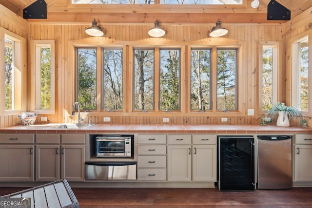 kitchen featuring tile countertops, beverage cooler, stainless steel refrigerator, and wooden walls