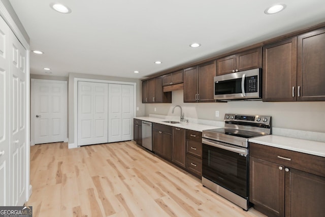 kitchen with light countertops, appliances with stainless steel finishes, light wood-style floors, a sink, and dark brown cabinets