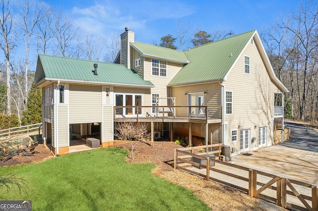 back of house featuring metal roof, a yard, french doors, a wooden deck, and a chimney