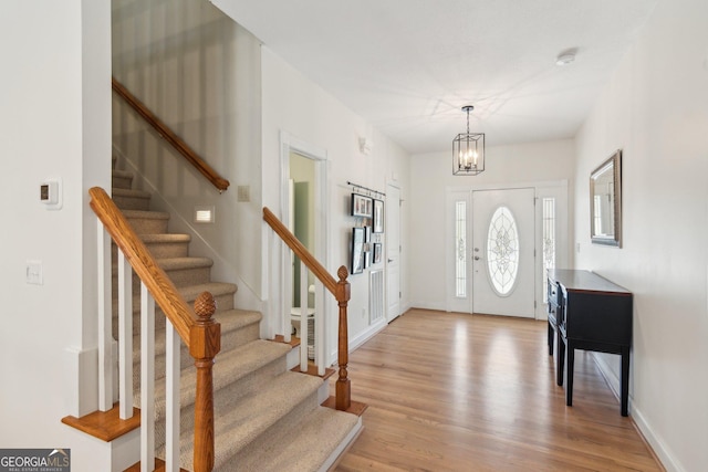 foyer with stairs, light wood finished floors, a chandelier, and baseboards