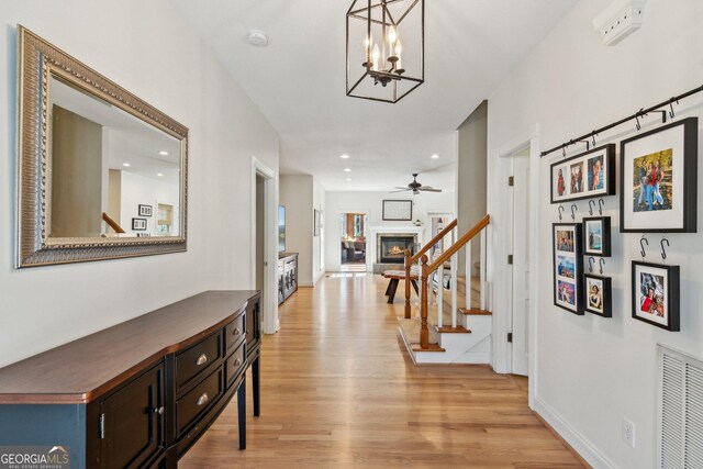 interior space with ceiling fan with notable chandelier, visible vents, baseboards, stairway, and light wood finished floors