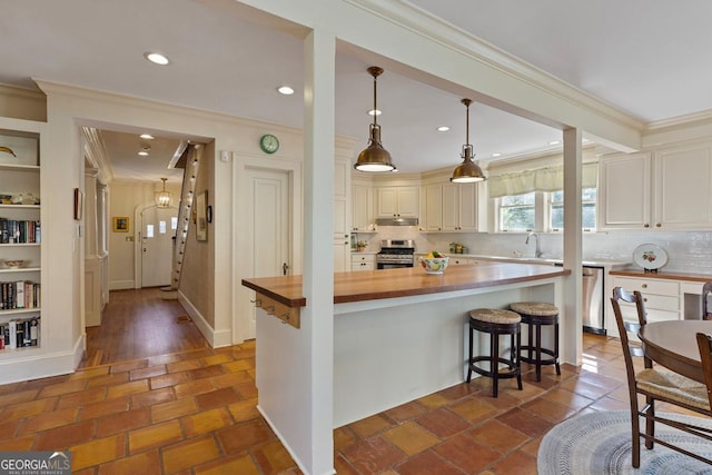 kitchen with stainless steel appliances, butcher block counters, ornamental molding, a kitchen island, and under cabinet range hood