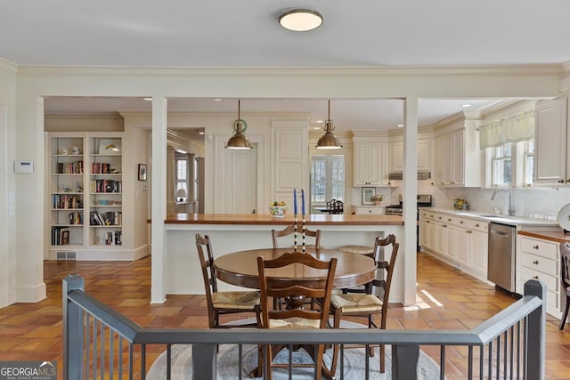 kitchen featuring plenty of natural light, decorative light fixtures, cream cabinetry, under cabinet range hood, and stainless steel dishwasher