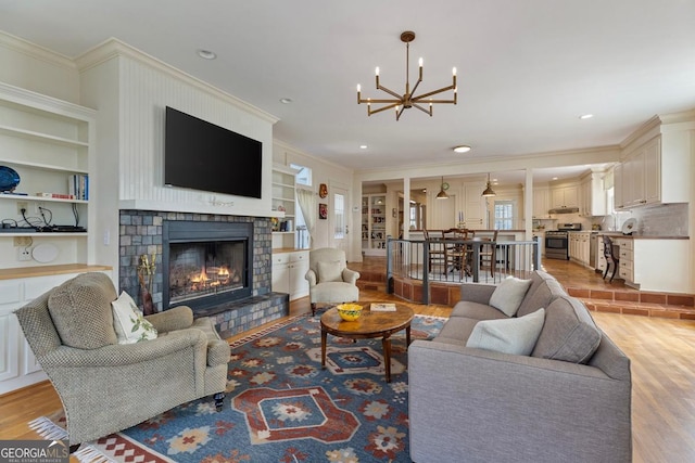 living room featuring a chandelier, recessed lighting, a lit fireplace, ornamental molding, and light wood finished floors