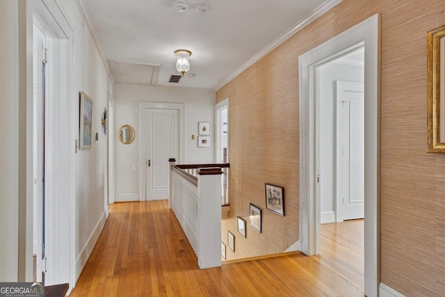 corridor with light wood-style flooring, an upstairs landing, baseboards, ornamental molding, and attic access