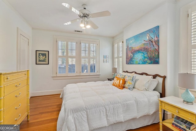 bedroom with light wood-style floors, visible vents, ornamental molding, and baseboards