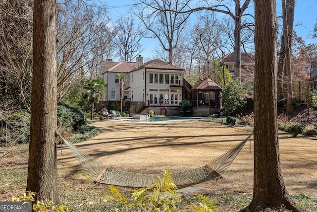 back of property with a chimney, an outdoor pool, and a gazebo