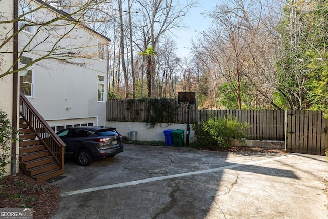 view of vehicle parking with driveway, stairway, an attached garage, and fence