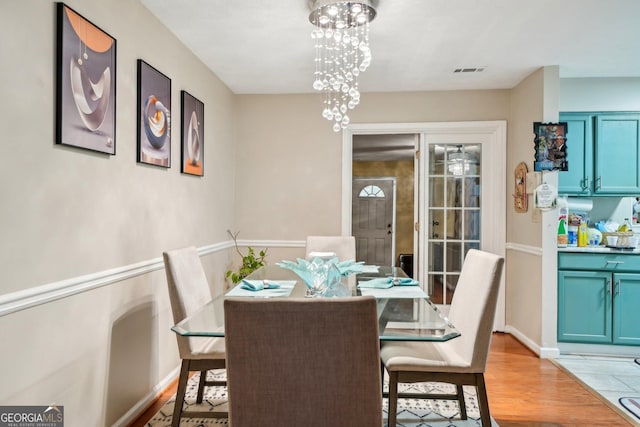 dining room with light wood-style floors, visible vents, baseboards, and an inviting chandelier