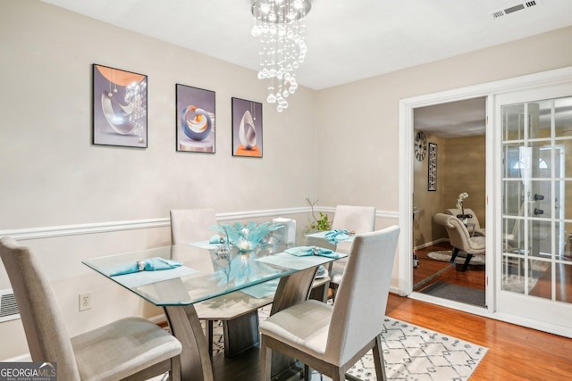 dining space with wood finished floors, visible vents, and a notable chandelier