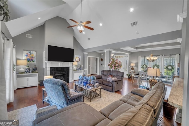 living area featuring ceiling fan with notable chandelier, dark wood-type flooring, a fireplace, visible vents, and decorative columns