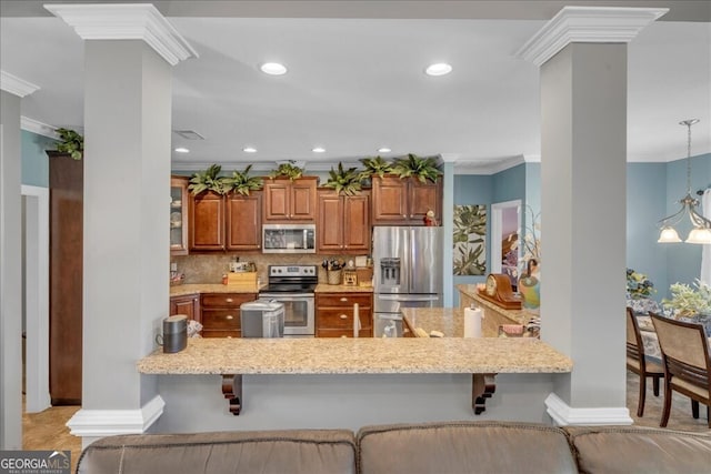 kitchen featuring decorative columns, appliances with stainless steel finishes, ornamental molding, a peninsula, and a kitchen bar